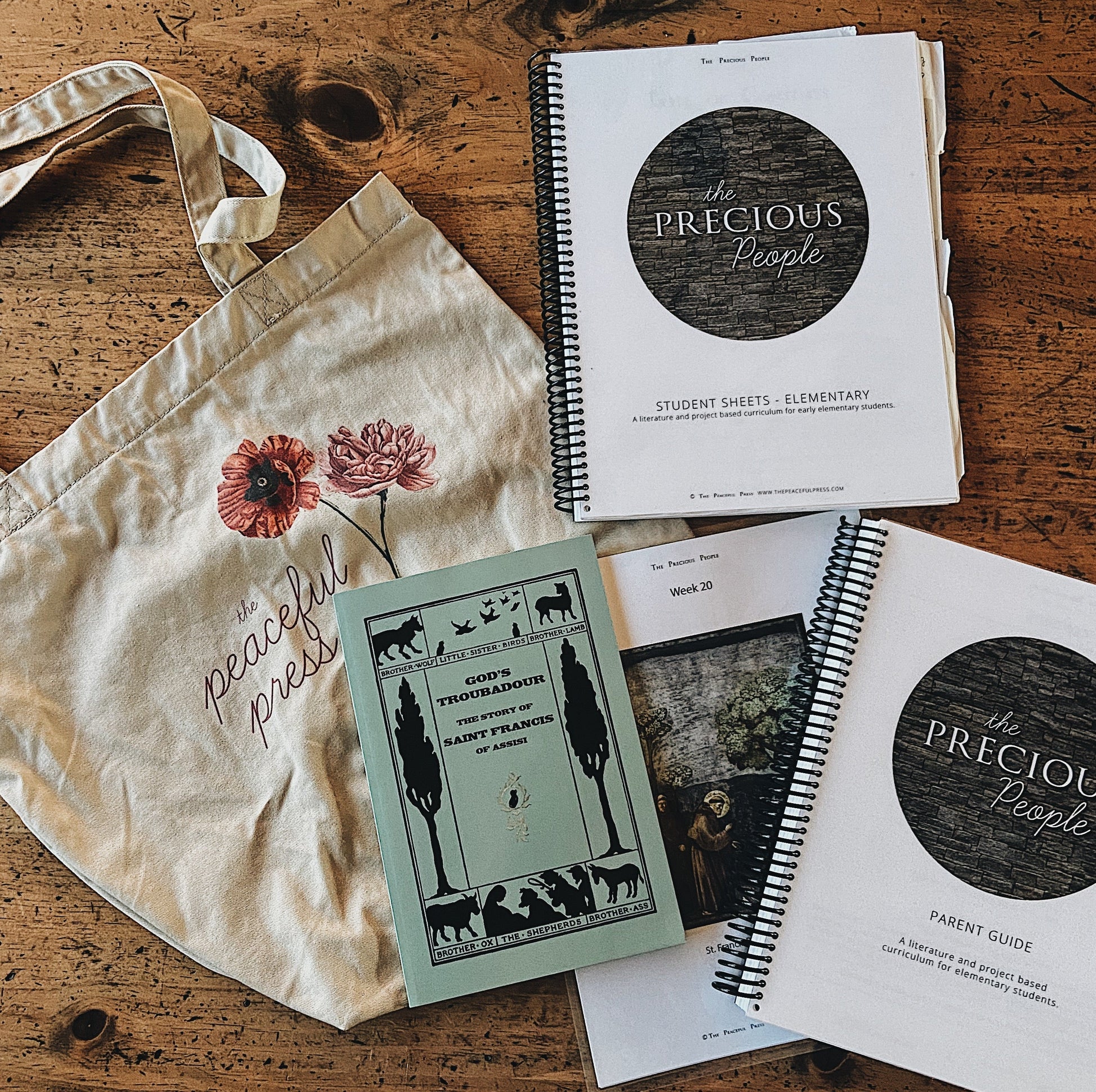 The Peaceful Press Eco Tote Bag next to the student and parent guide for the precious people homeschool curriculum books.