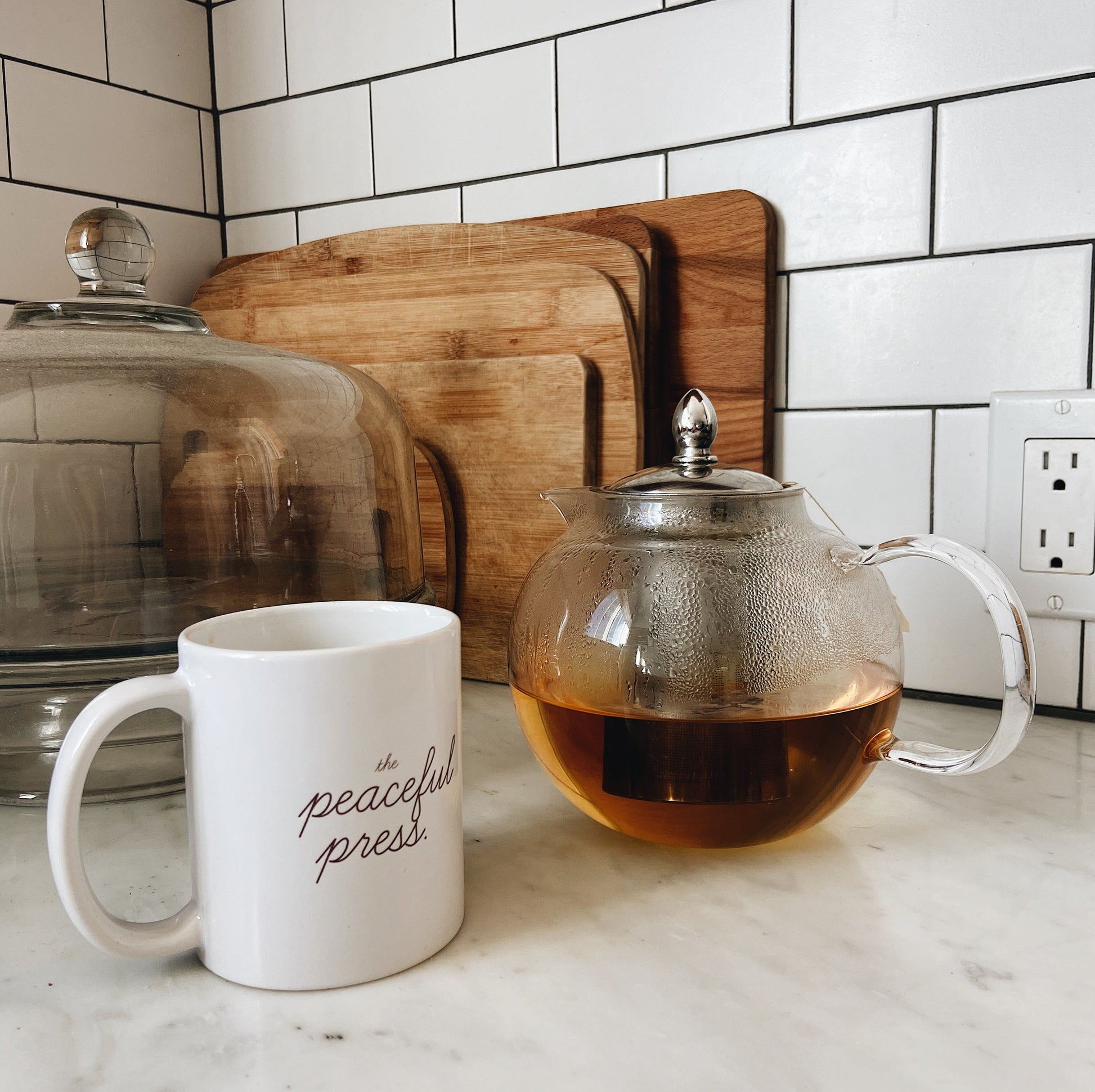 The Peaceful Press Logo on a white ceramic mug next too a tea pot.