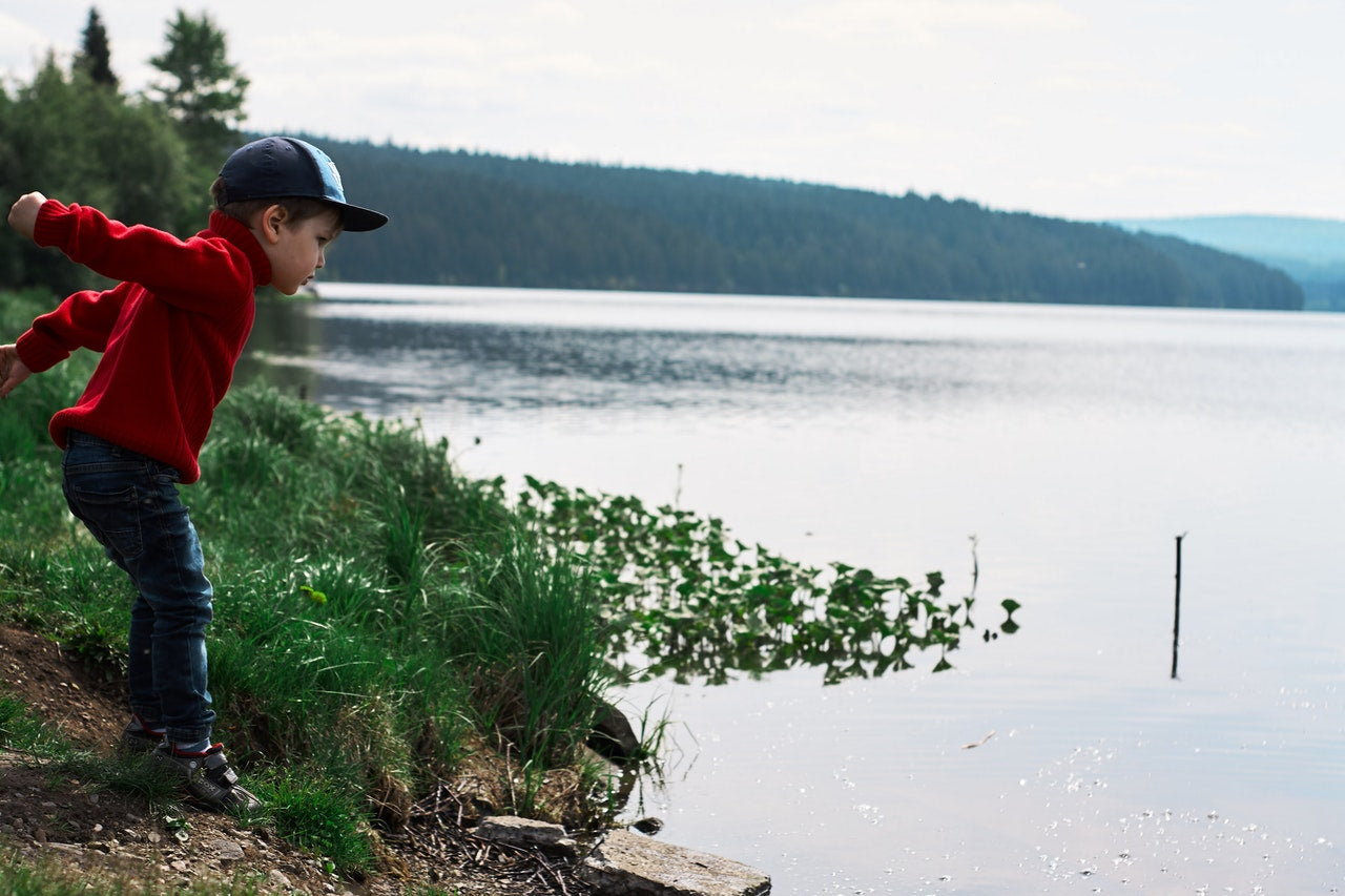 A homeschool kindergarten child throwing a rock in a lake.