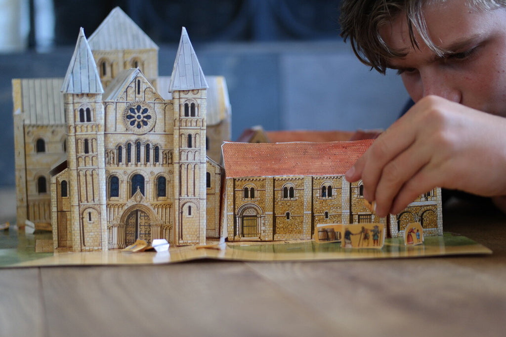 An image of a homeschooler playing with a paper model of Notre Dame Cathedral and villagers.