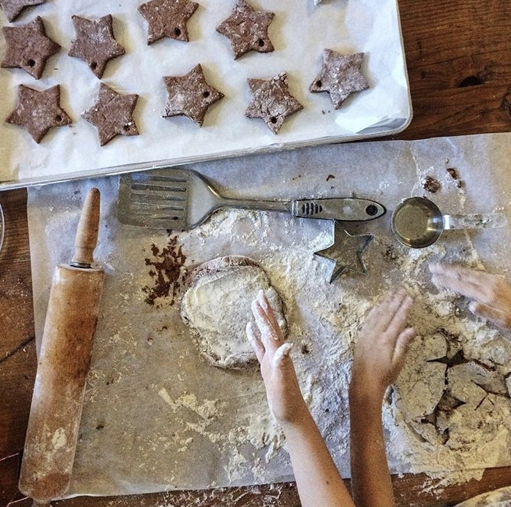 A homeschooler making star cookies, their hands covered in flower.