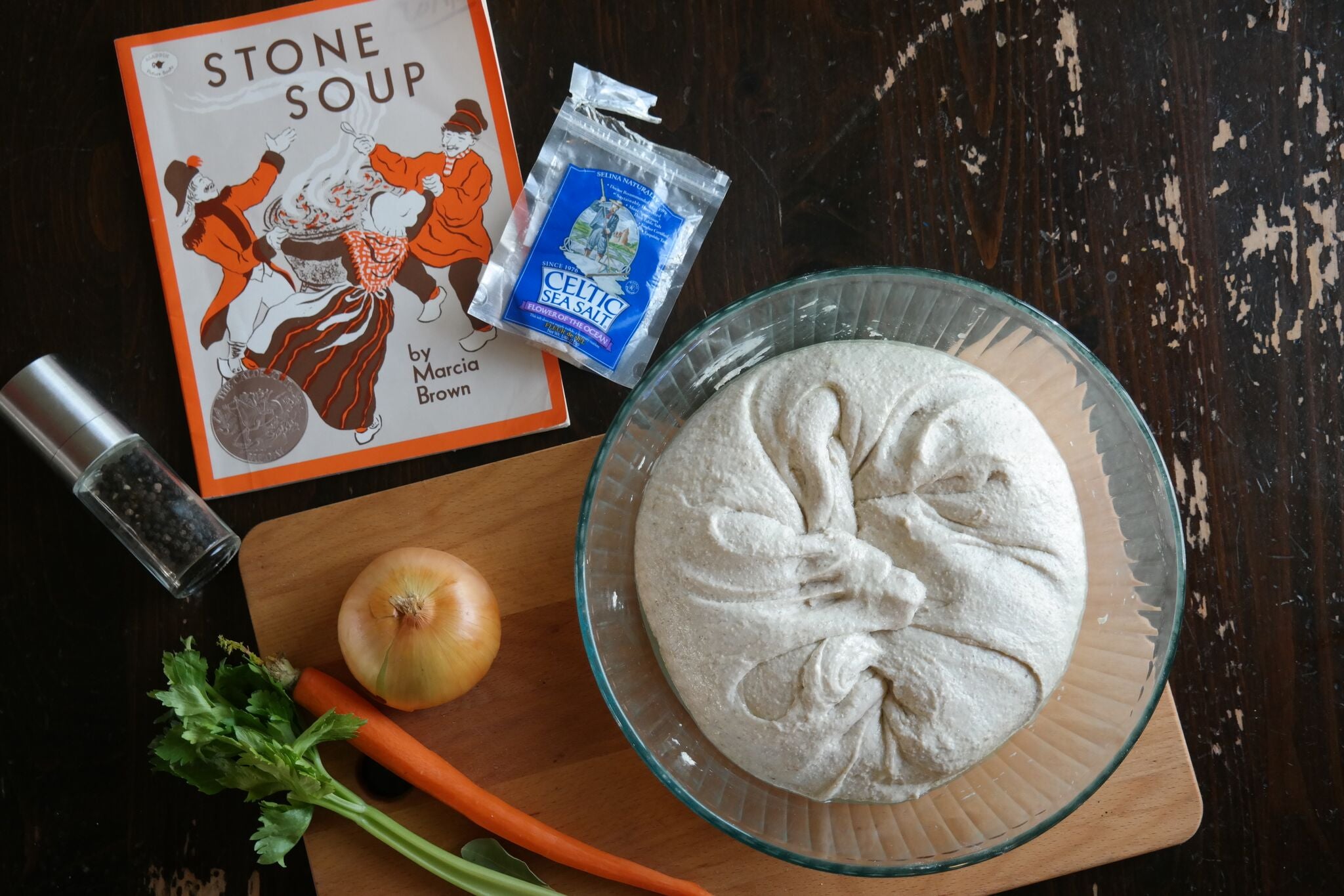 The book "Stone Soup" on a well worn wooden table next to a bowl of sour dough dough made by a homeschool family.