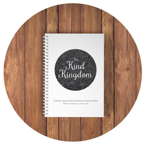 Spiral Bound Copy of the Kind Kingdom Homeschool Curriculum on a wooden background.