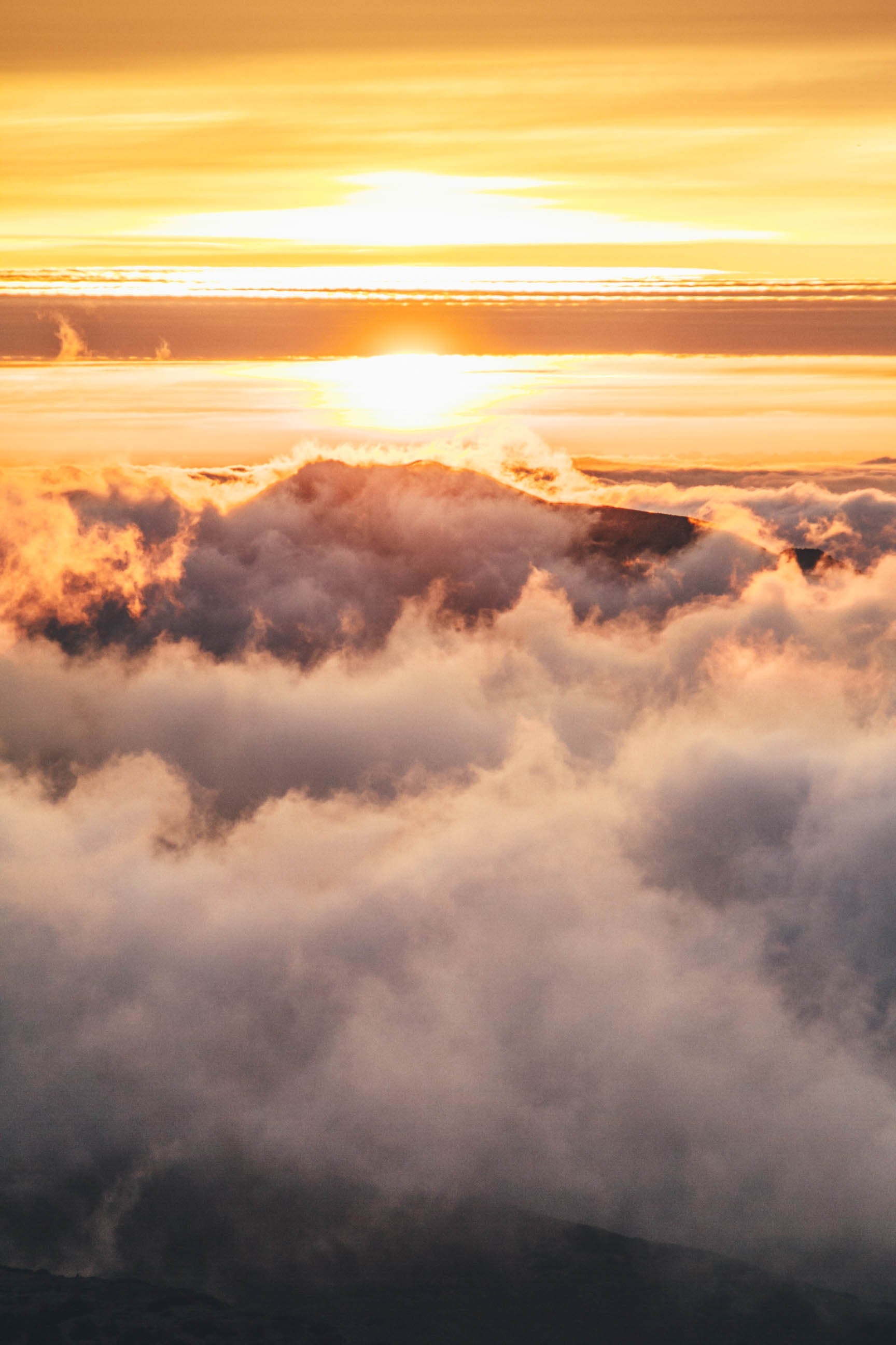 A photo of a sunrise over a majestic mountain range shrouded in clouds.